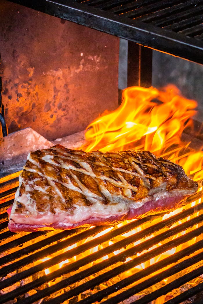 Close-up of a sizzling steak cooking on a grill with open flames, showcasing intense heat and searing marks.