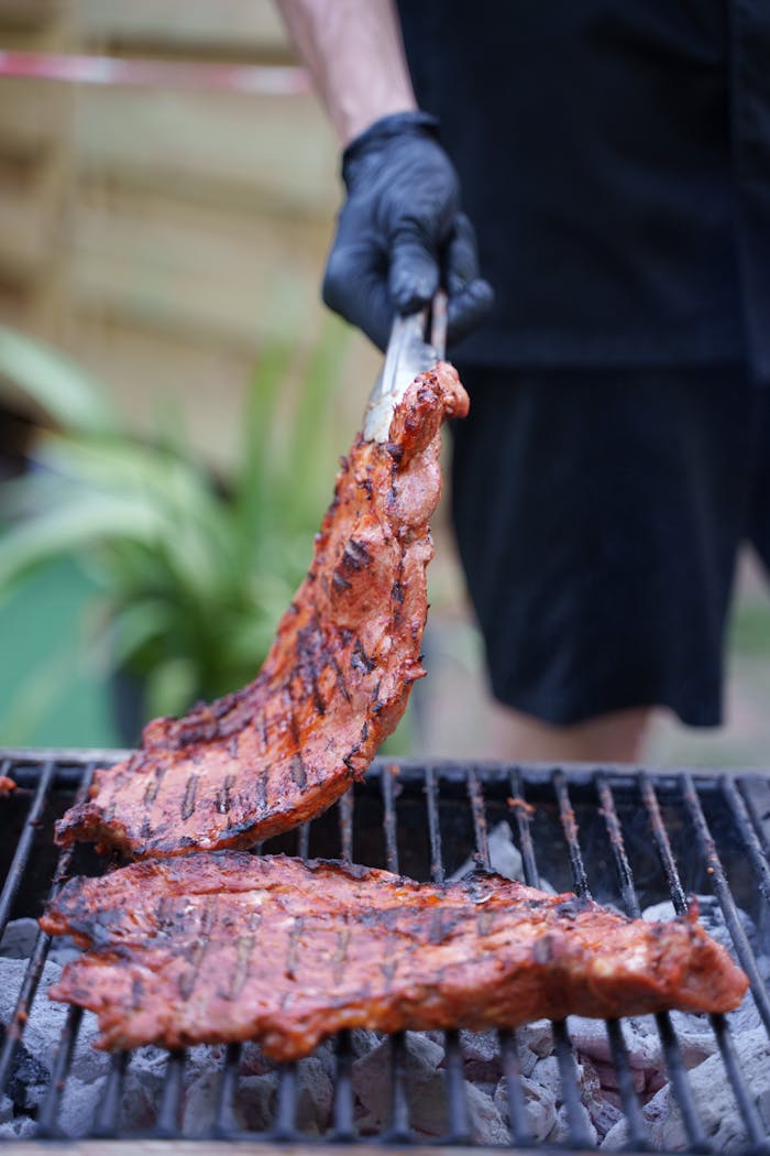 Close-up of seasoned ribs being cooked on a barbecue grill outdoors. Perfect for BBQ lovers.